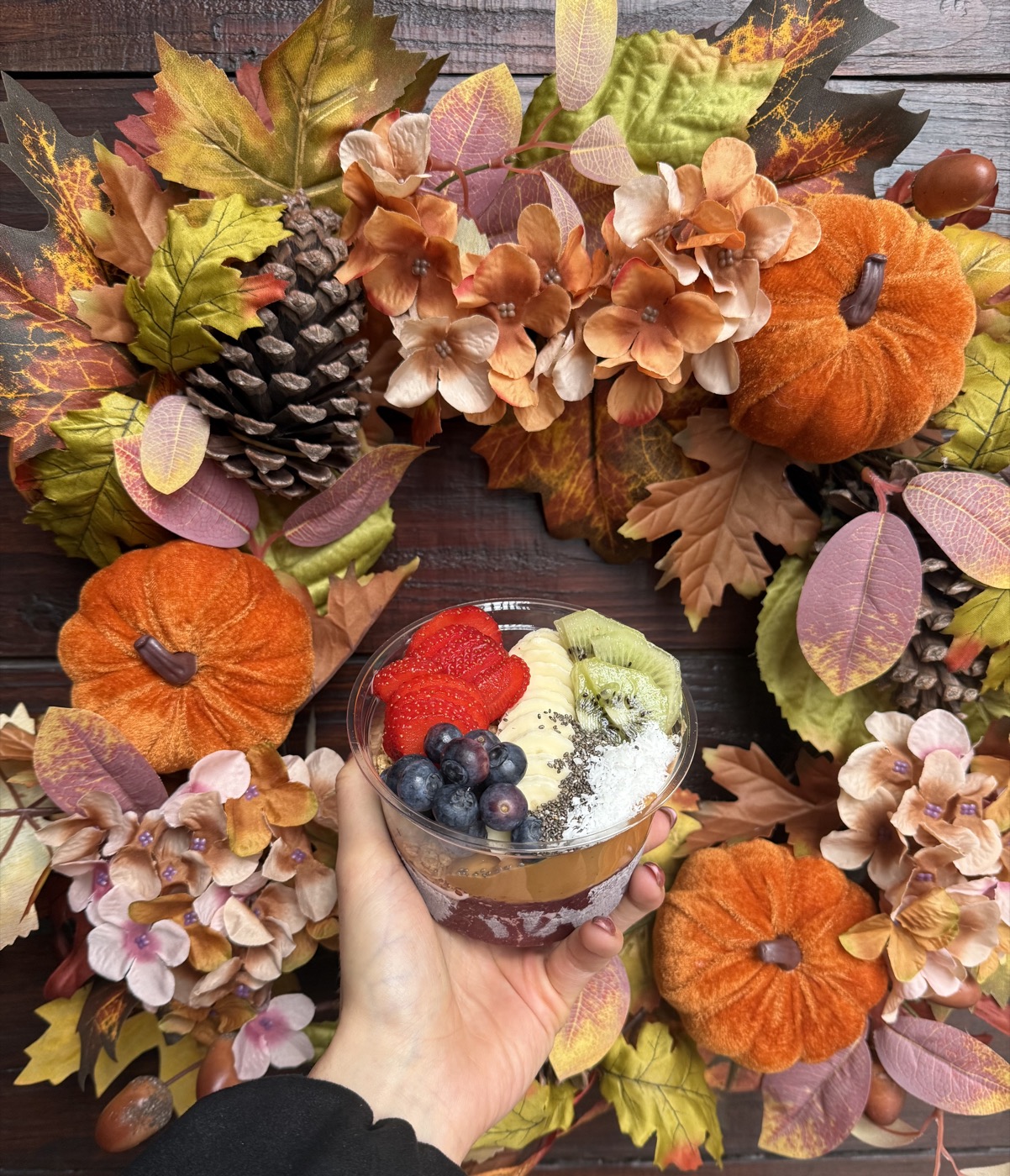 An açaí bowl held over an autumn wreath of pumpkins and leaves